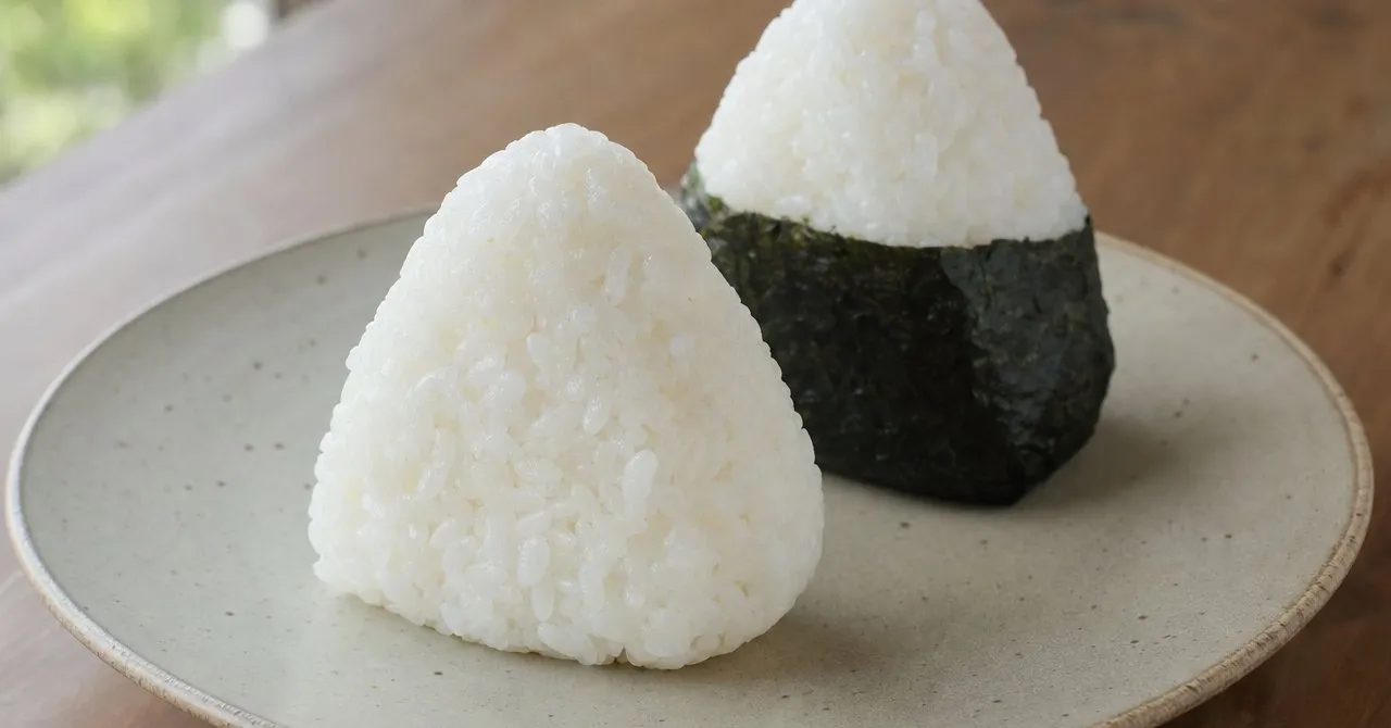 Two triangular onigiri of plain white rice, one wrapped with a strip of nori, on a simple plate.